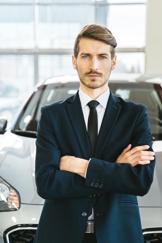 Professional businessman standing confidently in a car showroom wearing a suit and tie.